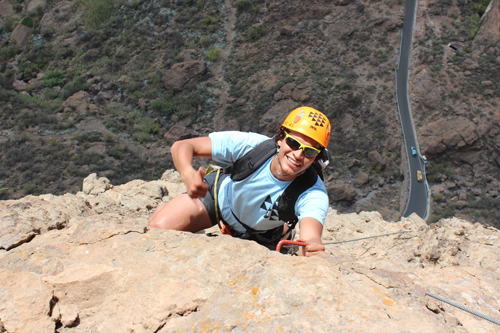 Ein junger Kletterer bewältigt eine Via Ferrata in Gran Canaria in 200 Metern Höhe, klettert an felsigen Klippen entlang und nutzt Sicherheitsausrüstung, während er die atemberaubende Aussicht auf die umliegende Landschaft genießt